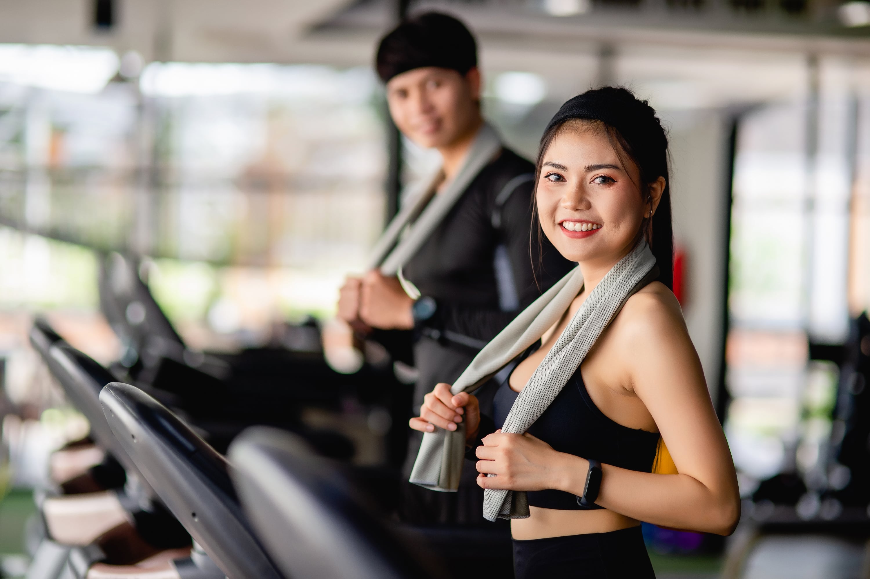 selective focus portrait sexy woman sportswear running treadmill blurred handsome man run nearly they are workout modern fitness gym smile copy space min